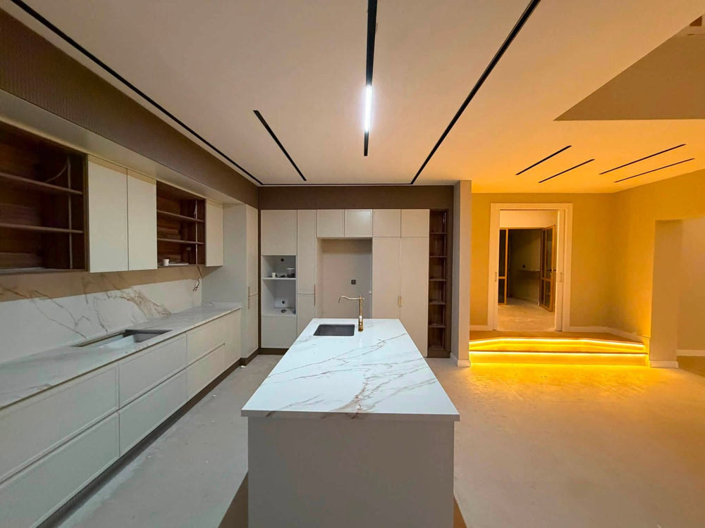 Villa mutfağı, uzun tezgâh hattı, evyeli ada, ceviz desenli raf nişleri ve lineer tavan aydınlatması